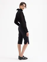 Pantalón capri estilo sastrero, color negro, de corte ajustado al cuerpo. Presenta alforzas en los delanteros, bolsillos ojales falsos y aberturas con tajo en los laterales inferiores.