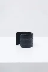 Pulsera rígida tipo brazalete de cuero en color crudo con textura efecto cocodrilo y costuras decorativas en los bordes.