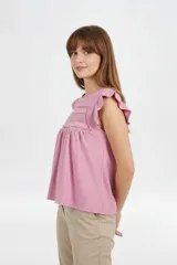Remera de algodón color rosado, de corte holgado y mangas cortas con volados, con detalle de encaje en el frente y cuello redondo a la base.