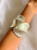 Brazalete rígido de diseño abierto, acabado en tono plateado con textura martillada y forma curva.