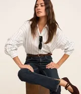 Pantalón de jean de corte slim, color azul oscuro, con trabillas en la cintura, cierre por botón y cremallera, bolsillos y aberturas en los bajos.