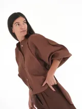 Camisa de lino blanca, de corte oversize, con mangas largas abullonadas, cuello mao y botones. Es más larga en la parte trasera e incluye un tajo en la espalda.