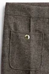 Pantalón de tiro alto en color marrón oscuro, con diseño de pierna recta y pliegues frontales cosidos. Presenta bolsillos de parche delanteros con botones decorativos dorados.