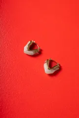 Aros tipo argolla de diseño escultórico y asimétrico, combinando metal dorado con resina en tono marmolado claro.