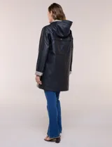 Pilot engomado impermeable color azul, de corte recto estilo trench con acabado resistente al agua. Cuenta con capucha integrada, cierre frontal con broches a presión, bolsillos laterales con ojal y forro interior de tela estampada a cuadros visible en la solapa y los puños.