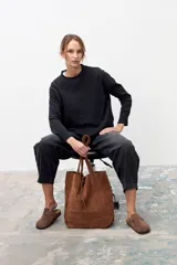 Bolso tipo tote de gran tamaño, confeccionado en gamuza color tostado. Presenta un diseño minimalista con doble asa larga para llevar al hombro y un cierre mediante cordón ajustable en la parte superior.