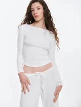 Remera de manga larga entallada confeccionada en tejido pointelle suave. Presenta escote a la base con un pequeño detalle de lazo central y acabado picot en los bordes. Su diseño es flexible y liviano, adaptándose al cuerpo.