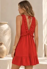 Vestido corto negro con escote en V, sin mangas y detalles de volados en el pecho y en el borde inferior.