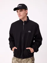 Campera Rusty de corte clásico, color negro, con cierre frontal completo, cuello alto y puños elásticos. Presenta un diseño minimalista con el logo de la marca bordado en el pecho.