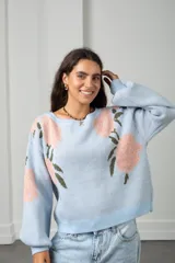 Buzo de punto color celeste con estampado de flores rosadas y hojas verdes. Presenta cuello redondo, mangas largas tipo globo y diseño holgado oversize.