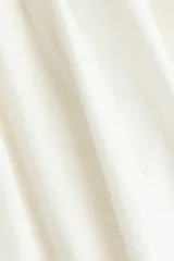 Vestido midi blanco de popelina de algodón, con cuerpo fruncido tipo nido de abeja, escote cuadrado y tirantes anchos con volantes que se cruzan en la espalda. Falda con ligero vuelo.