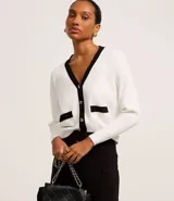 Cardigan de punto blanco con escote en V, botones metalizados, bolsillos falsos, cuello y vista contrastantes en negro, y bajo acanalado.