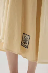 Vestido midi de lino color salmón, de corte amplio y silueta holgada. Presenta diseño con cortes irregulares y detalles de pasamanería en el escote y costuras. Cuenta con breteles dobles tipo cuerda y ruedo asimétrico.