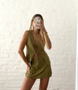 Conjunto de dos piezas color verde oliva con textura arrugada. Incluye un chaleco sin mangas con cierre frontal de lazos y una minifalda ajustada.