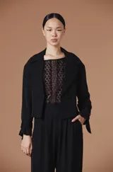 Blusa de encaje blanco con diseño floral geométrico, cuello redondo y mangas largas abullonadas con puños ajustados.