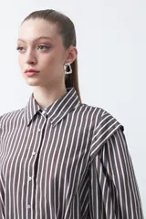 Camisa a rayas azules y blancas de manga larga, con cuello clásico y puños abotonados. Presenta un diseño entallado en la cintura.