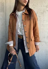 Chaqueta de gamuza color camel, con corte recto, cuello camisero, cierre frontal con botones metálicos y bolsillos frontales con solapa.