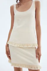 Pollera mini de tejido bouclé color crema, de tiro alto con elástico oculto en la cintura y bajo desflecado.