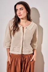 Cardigan de algodón peinado color beige, con cuello camisero, cierre frontal de botones y detalles de textura en crochet con diseño de flores. Mangas tres cuartos y diseño corto.