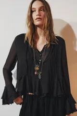 Camisa de viscosa con cuello redondo y escote en pico ajustable mediante lazadas. Presenta cierre frontal con botones, mangas largas con terminación evasé y detalle de volantes en el mismo tejido.