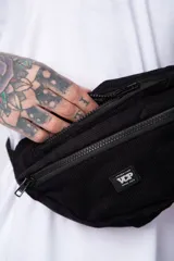 Riñonera de corderoy color negro, con compartimento principal y bolsillo frontal con cierre, tira ajustable con hebilla plástica y detalle de parche bordado con la marca VCP.