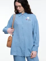 Camisa celeste de calce relajado con abertura en la espalda y mangas largas. Confeccionada en tejido liviano de lino y viscosa. Incluye tres pins decorativos.