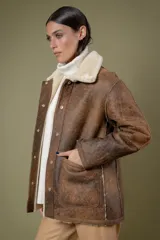 Campera tipo borrego de cuero con efecto desgastado, con interior y cuello de piel sintética en color crema. Presenta cierre frontal con botones a presión y bolsillos frontales amplios.