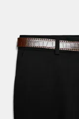 Pantalón de tiro alto color negro, de corte recto y pinzas frontales. Incluye un cinturón delgado de cuero marrón con hebilla metálica dorada.