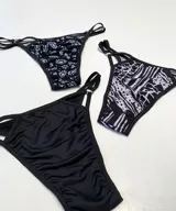 Pack de tres bombachas colaless con tiras finas y argollas metálicas. Incluye una bombacha negra lisa, una con estampado de flores blancas y otra con estampado abstracto en blanco y negro.