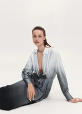 Vestido camisero midi de tejido satinado y fluido con efecto degradado. Presenta cuello camisero, escote en pico, mangas largas con puños abotonados, diseño drapeado en la cintura y bajo asimétrico.