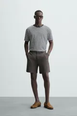 Bermuda de hombre color beige claro, corte regular fit, con pliegues frontales, bolsillos delanteros y bolsillos traseros de doble vivo con botón.