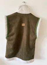 Chaleco negro de cuerina con interior de corderito sintético, bolsillos frontales y hebillas decorativas.