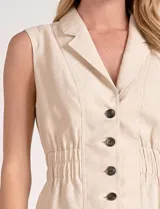 Chaleco entallado color beige, con cuello solapa tipo sastre, escote en V y cierre frontal con botones en contraste. Presenta cintura elastizada que define la silueta con un ligero vuelo en el ruedo.
