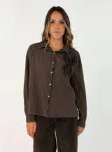 Camisa de corte oversize color beige, con cuello clásico, cierre frontal de botones y detalle de flores de tela aplicadas en el pecho.