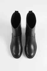 Botas de caña alta color negro, confeccionadas en cuero vegano, de diseño clásico y cómodo con suela plana y presilla en el talón.