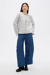 Saco de punto color gris, con cuello redondo, cierre frontal con botones y detalle de volados en la tapeta y el ruedo. Presenta mangas largas con puños acampanados.