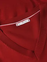 Sweater Tommy Hilfiger de punto fino en color rojo, con cuello en V y manga larga. Presenta un diseño liso con el logo de la marca bordado en el pecho y detalle de rayas distintivas en el interior del cuello.