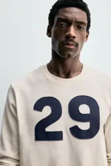 Camiseta relaxed fit de algodón con estructura waffle, color beige. Presenta un parche con el número "29" en azul marino en el pecho. Tiene cuello redondo y manga larga con acabados en rib.