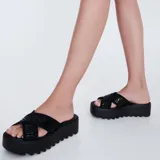 Sandalias Melissa modelo Cozy Slide de color negro, con plataforma gruesa dentada y tiras cruzadas de tela con el logotipo de la marca.