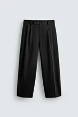 Pantalón negro de corte relaxed fit y estilo wide leg, con pliegues frontales dobles, bolsillos delanteros y detalle de bolsillos traseros de vivo. Cierre frontal cruzado con cremallera y gancho metálico oculto.