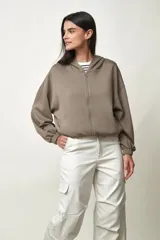 Campera Moana estilo hoodie con cierre frontal completo, capucha y bolsillos laterales, confeccionada en tejido verde grisáceo de corte oversize con mangas abullonadas y puños elásticos.