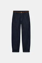 Pantalón de mezclilla azul oscuro, de tiro bajo, pernera recta y bajo con vuelta. Incluye un cinturón trenzado marrón con hebilla metálica.
