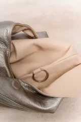 Bolso de hombro color beige, confeccionado en cuero sintético con interior plateado. Presenta un bolsillo externo con cierre.