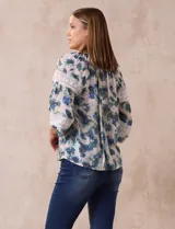 Blusa estampada con flores azules y verdes, cuello a la base con escote en V y volados. Manga larga con puño y apliques de puntilla.
