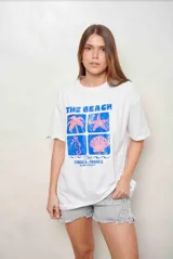 Remeron de algodón blanco con cuello redondo y mangas cortas. Presenta un estampado frontal con la inscripción 'THE BEACH CLUB CORSICA FRANCE' y gráficos playeros en tonos azules y rosados.