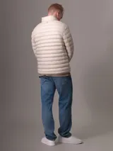 Campera acolchada color beige claro, con cuello alto y cierre frontal con cremallera. Tiene bolsillos laterales y logo de Calvin Klein en el pecho.