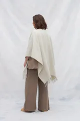 Ruana de lana 100% sin teñir en color tostado, con diseño de punto acanalado y terminación de flecos en el ruedo.