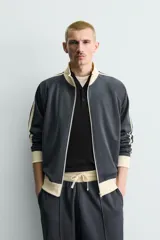 Sudadera de corte relajado en color azul marino con cuello alto y cierre frontal de cremallera. Presenta bandas laterales en color crema a contraste que recorren las mangas, puños y bajo en tejido rib, y bolsillos laterales de vivo.