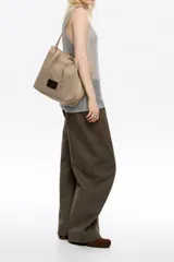 Bolso shopper mediano de tejido de punto color beige, con doble asa corta de mano y una correa larga ajustable para el hombro. Incluye parche con logo en la parte frontal.