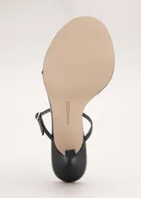 Sandalias de tacón alto color negro, con diseño minimalista de tiras finas cruzadas en el empeine y cierre con hebilla en el tobillo.